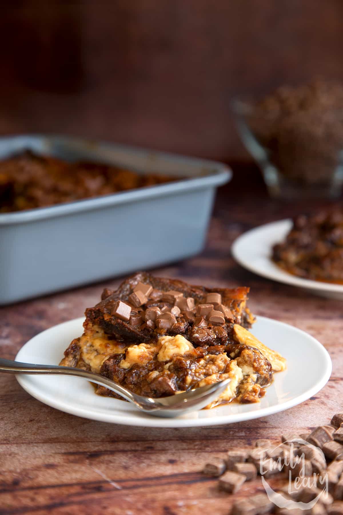 Malt loaf bread and butter pudding on a white plate with a spoon on the side.