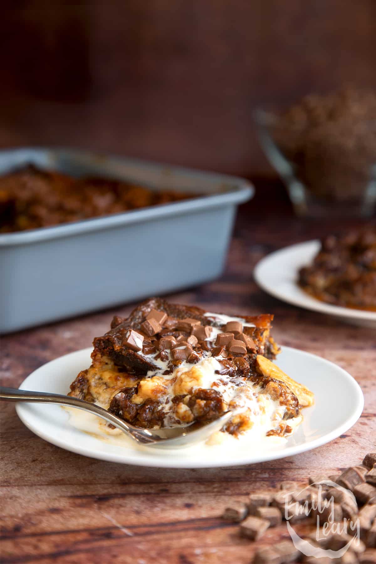 Malt loaf bread and butter pudding on a white plate topped with cream and a spoon on the side.