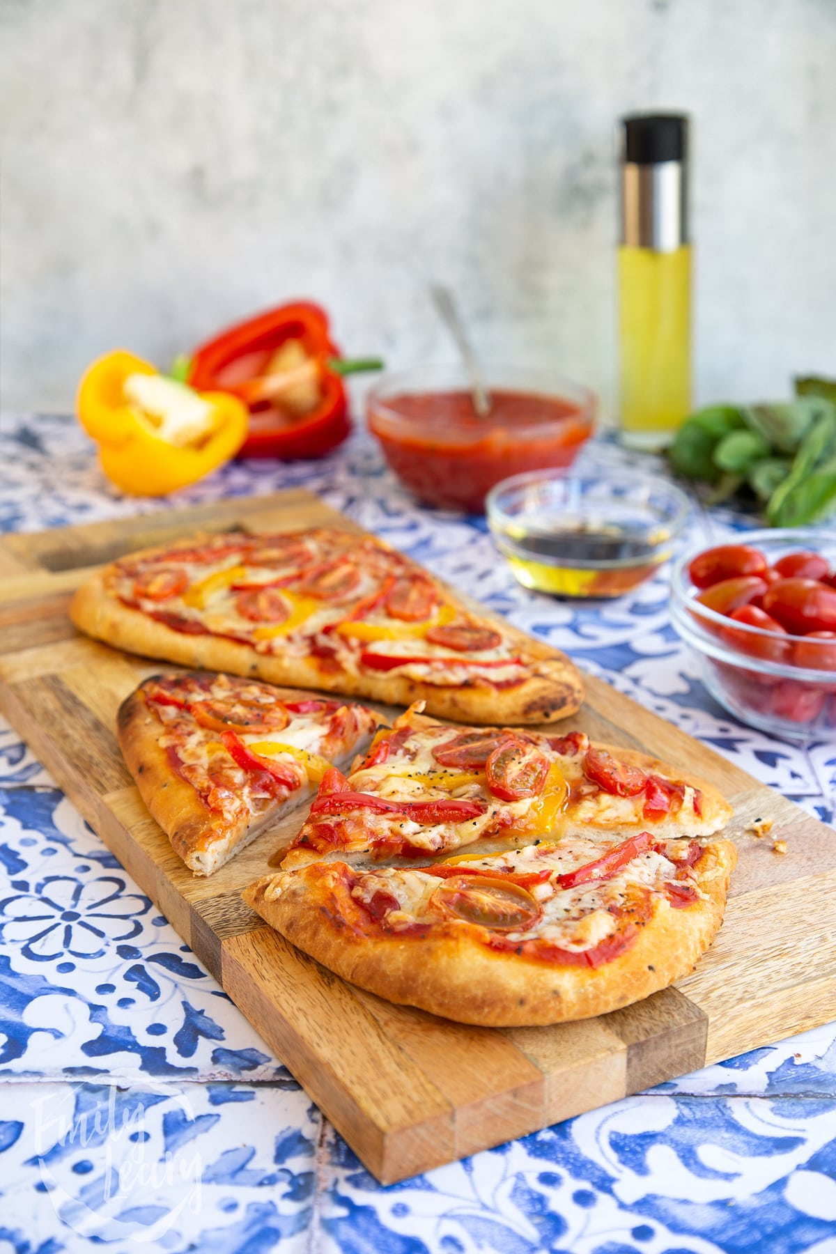Side on shot of two naan bread pizzas ontop of a wooden chopping board which has been placed on some blue and white decorative tiles.