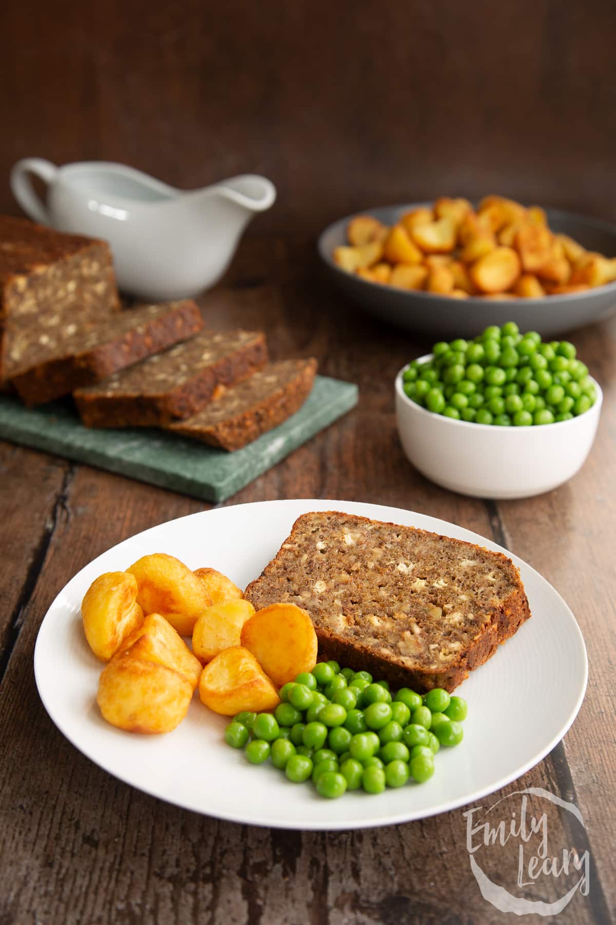 Side on shot of the special k loaf served on a plate with roast potatoes and peas.
