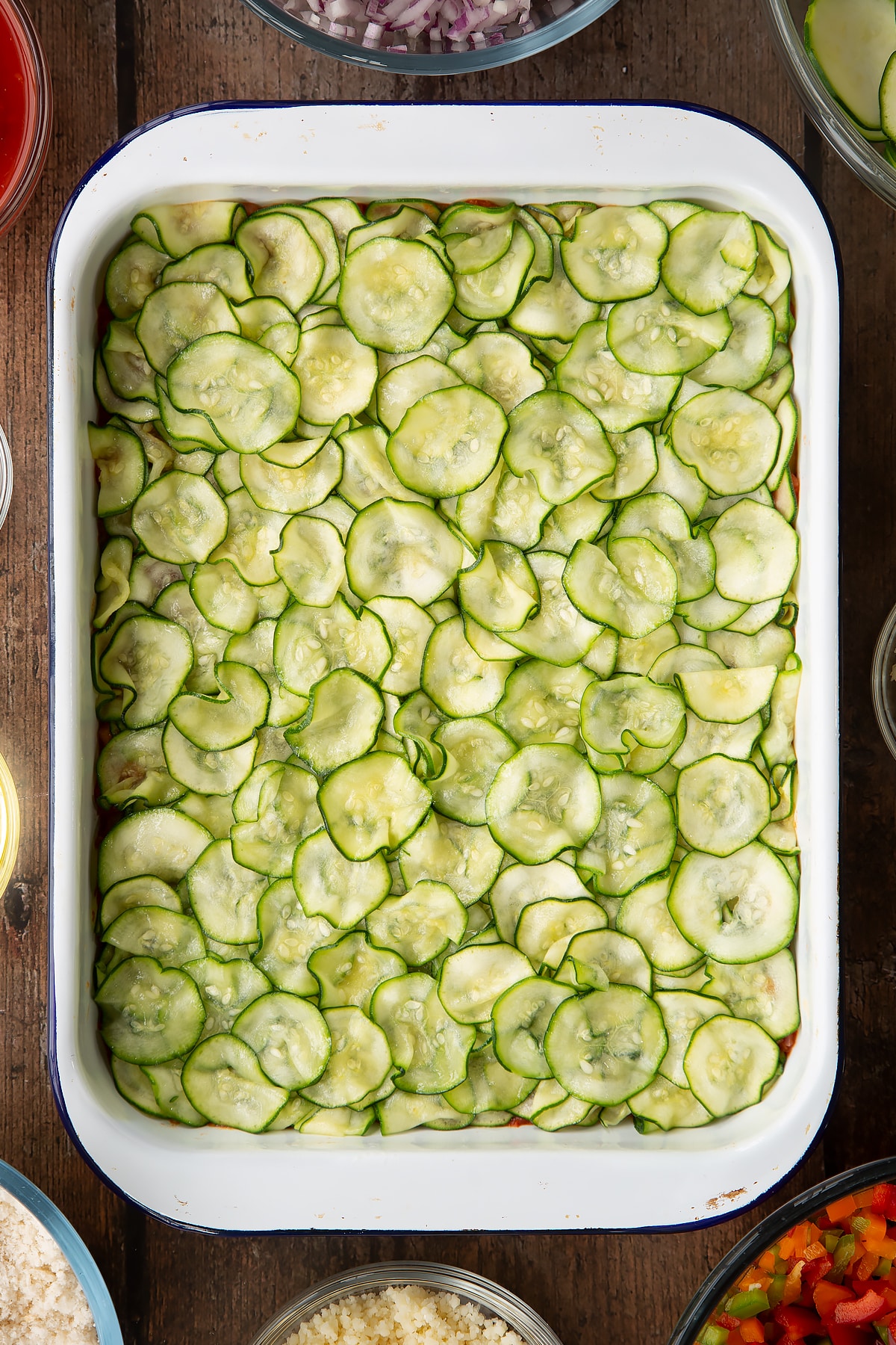 thinly sliced courgettes topping a tomato base in a white baking dish.