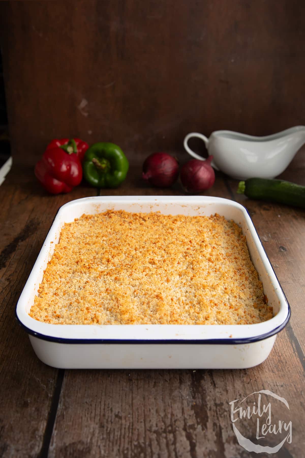 cooked tomato and courgette gratin in a white baking dish on a wooden background.