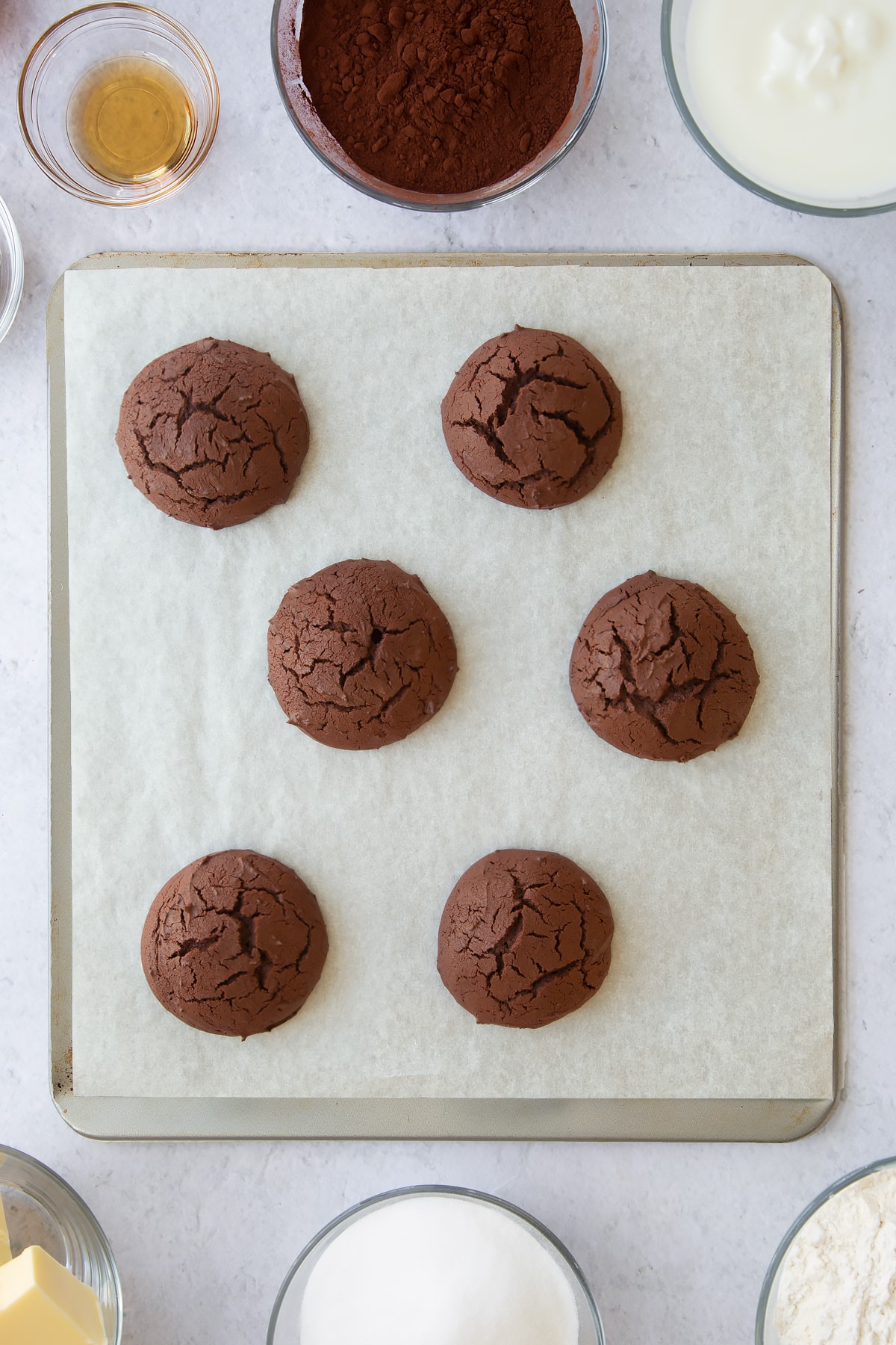 6 baked chocolate whoopie cookies on a parchment lined baking tray.