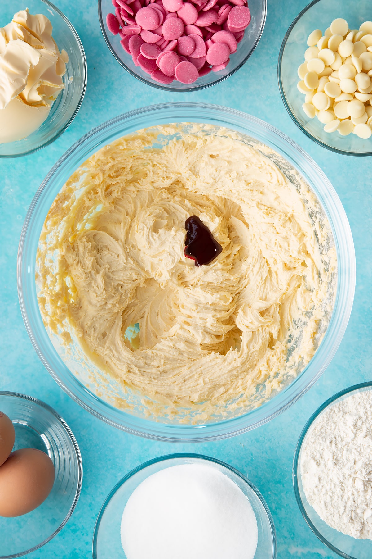 whisked margarine, sugar, eggs and flour in a large clear bowl topped with a small dollop of pink food colouring.