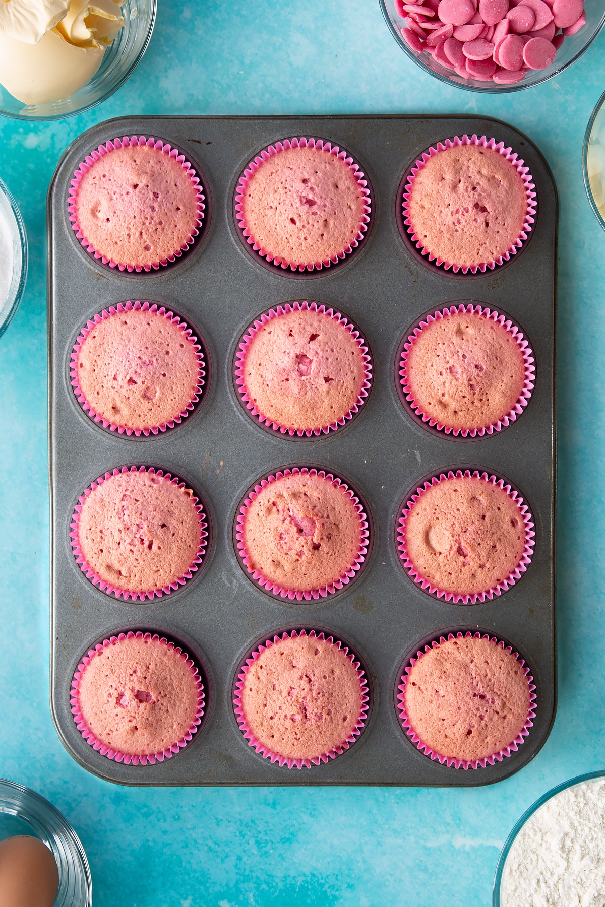12 pink cupcake liners filled with baked pink cupcake mix in a cupcake tray.