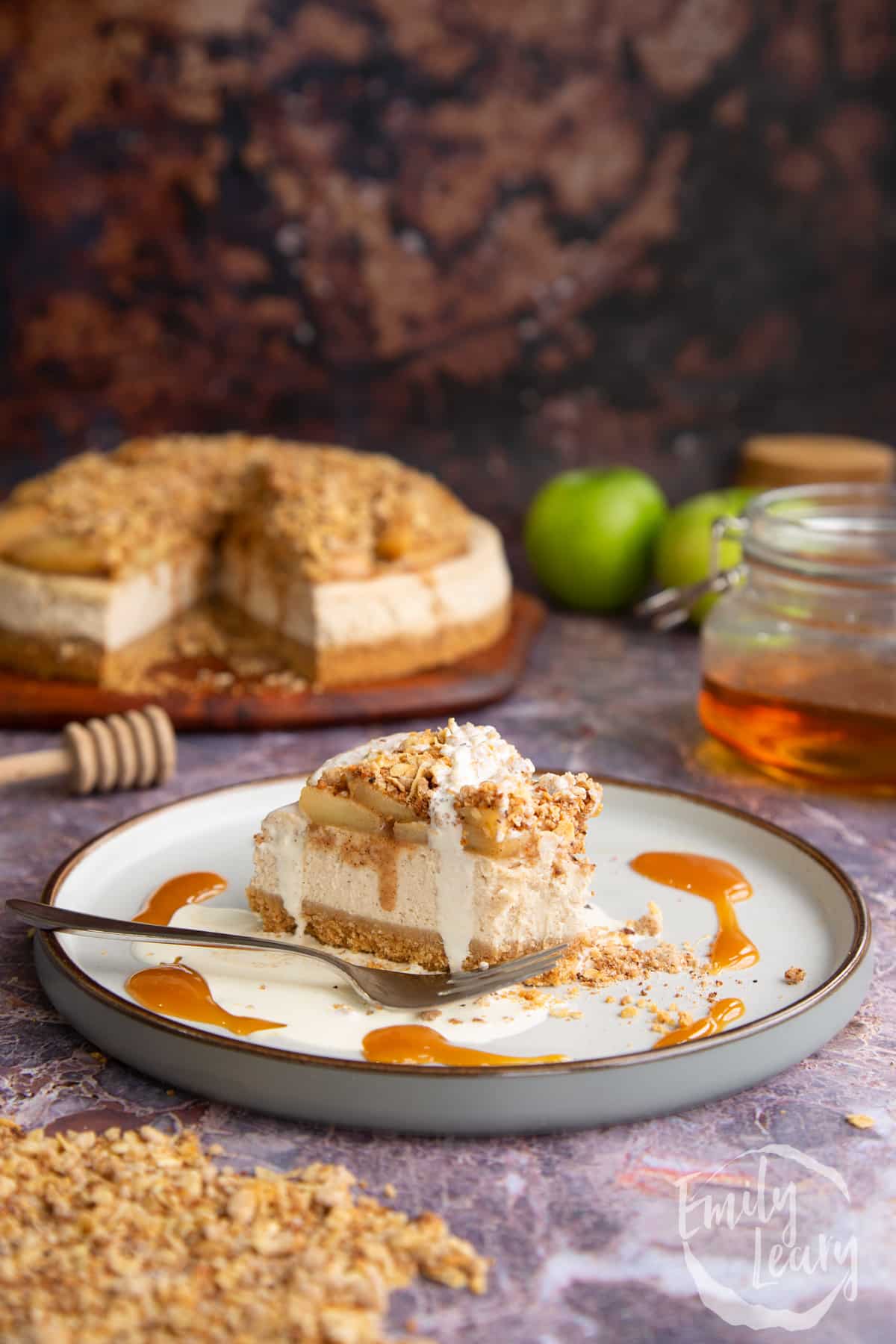 Side on shot of a slice of the finished apple crumble cheesecake with a bite taken out.