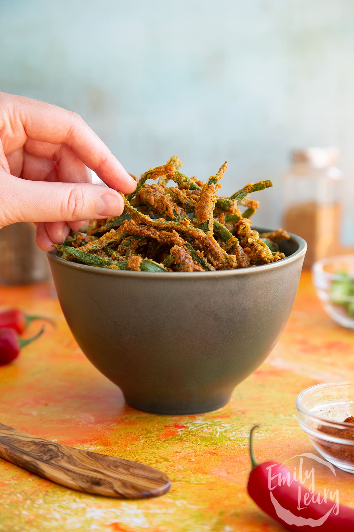 Hand reaching in to grab some kurkuri bhindi out of a dark bowl.