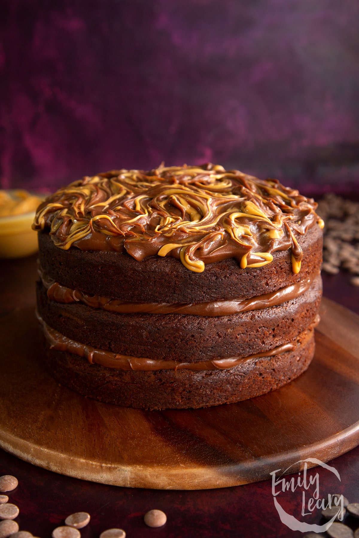 side view of a triple layer cake with chocolate peanut butter ganache on a wooden chopping board.