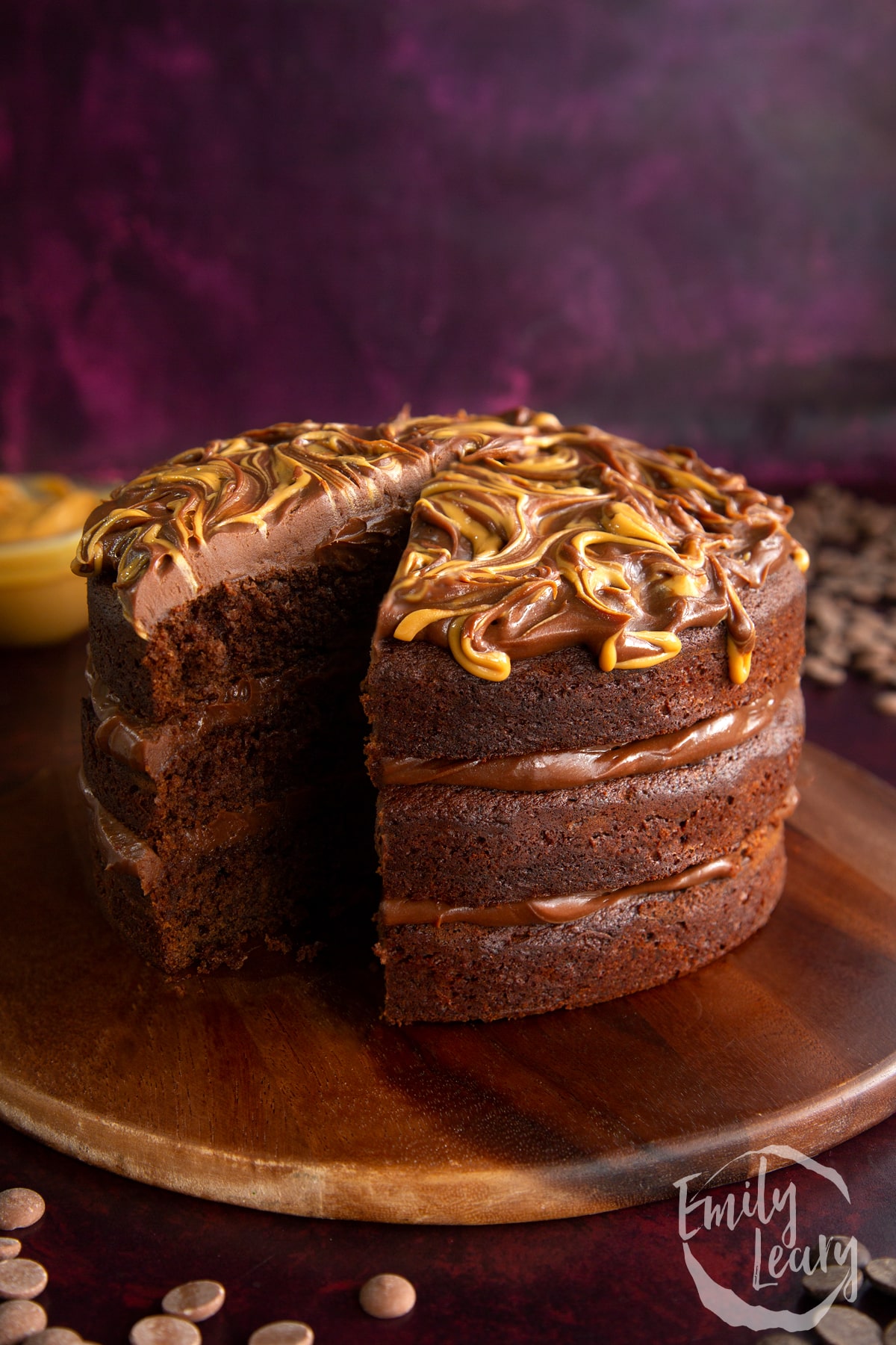 Peanut butter fudge cake with a slice cut out on a wooden chopping board.