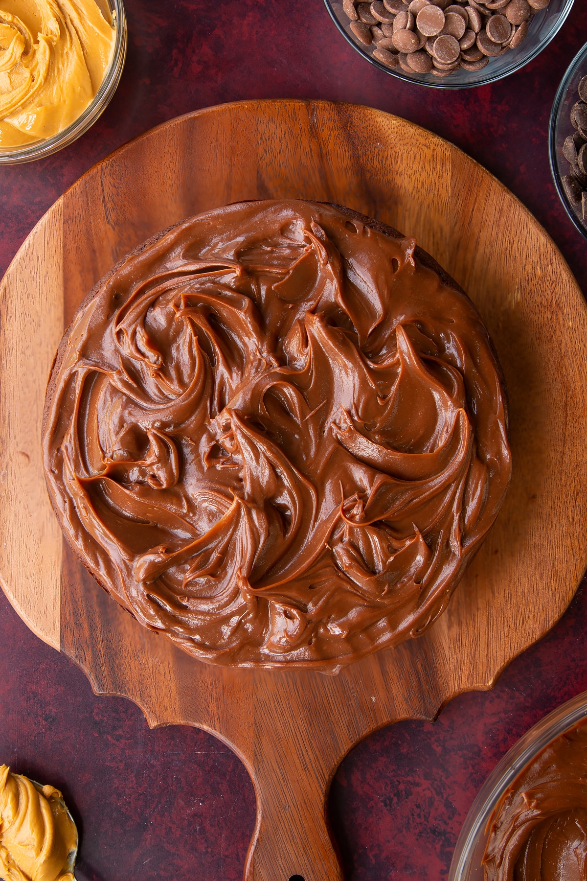 a cooked chocolate peanut butter cake topped with chocolate ganache on a wooden chopping board.
