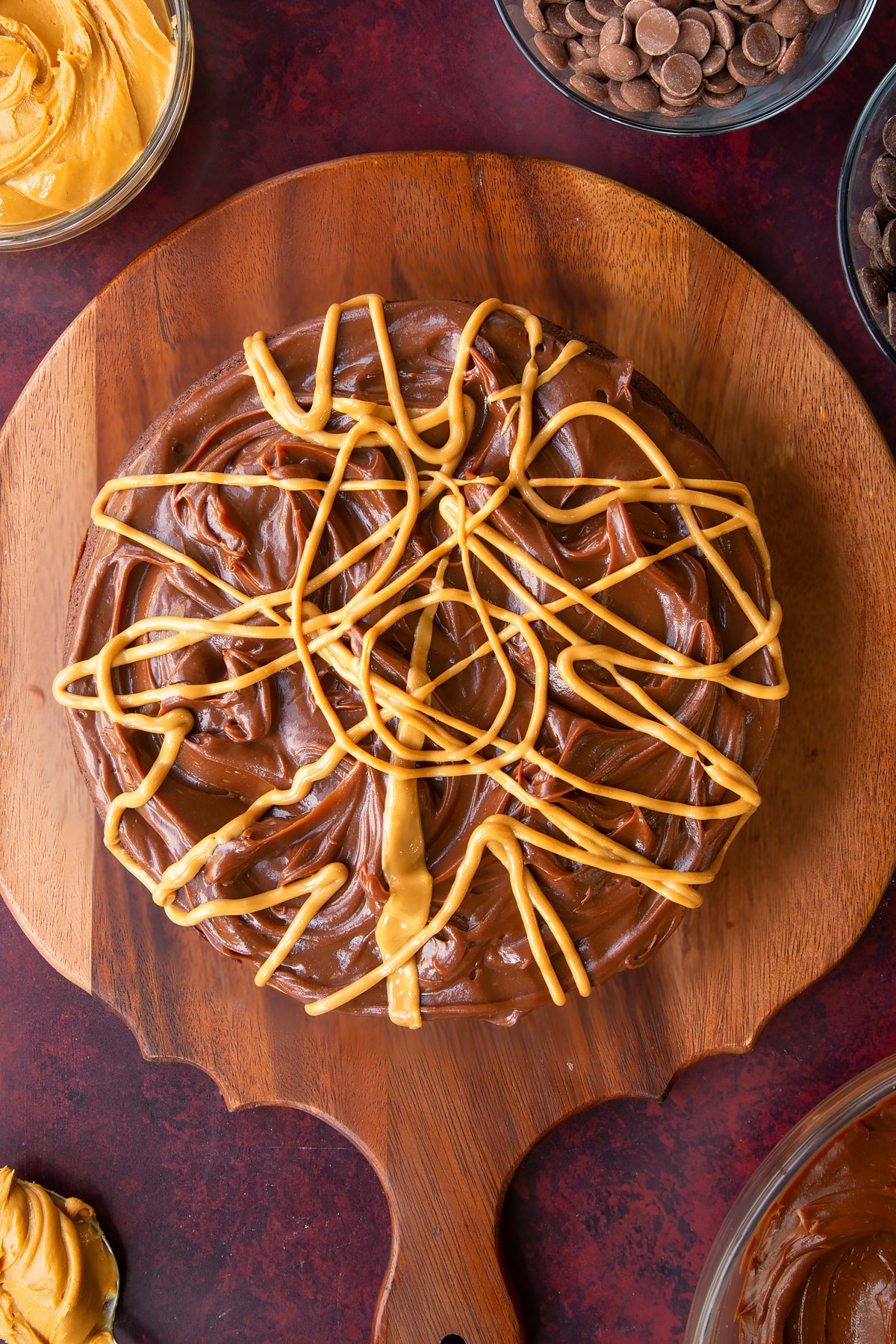 chocolate peanut butter ganache topped cake drizzled with peabut buteer on a wooden chopping board.