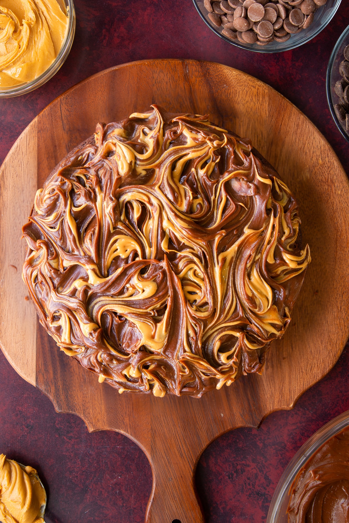 chocolate peanut butter ganache topped cake drizzled with peabut buteer on a wooden chopping board.