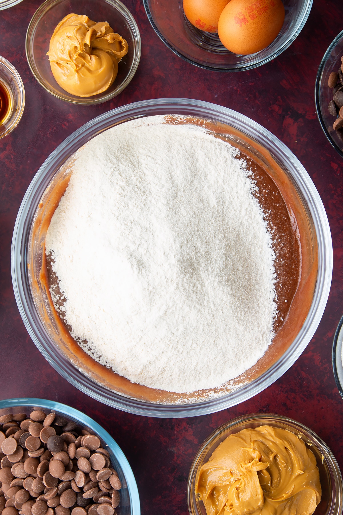 mixed chocolate peanuty butter batter topped with flour and bicarbonate soda in a large clear bowl.