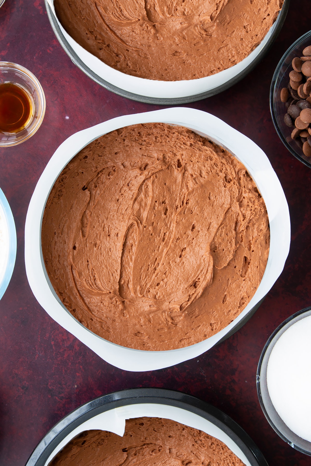 chocolate peanut butter cake batter divided into 3 cake tines with beaking paper around the edges.