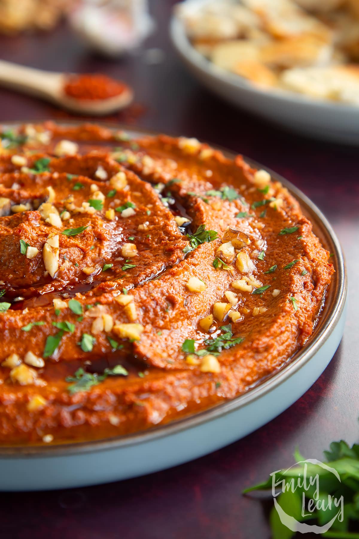 a side view of red pepper dip in a clear bowl topped with herbs and crushed walnuts.