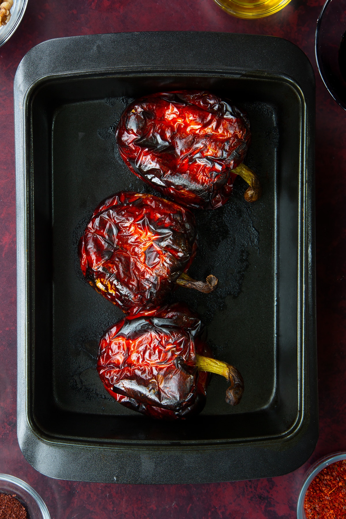 3 whole roasted red peppers in a roasting dish.