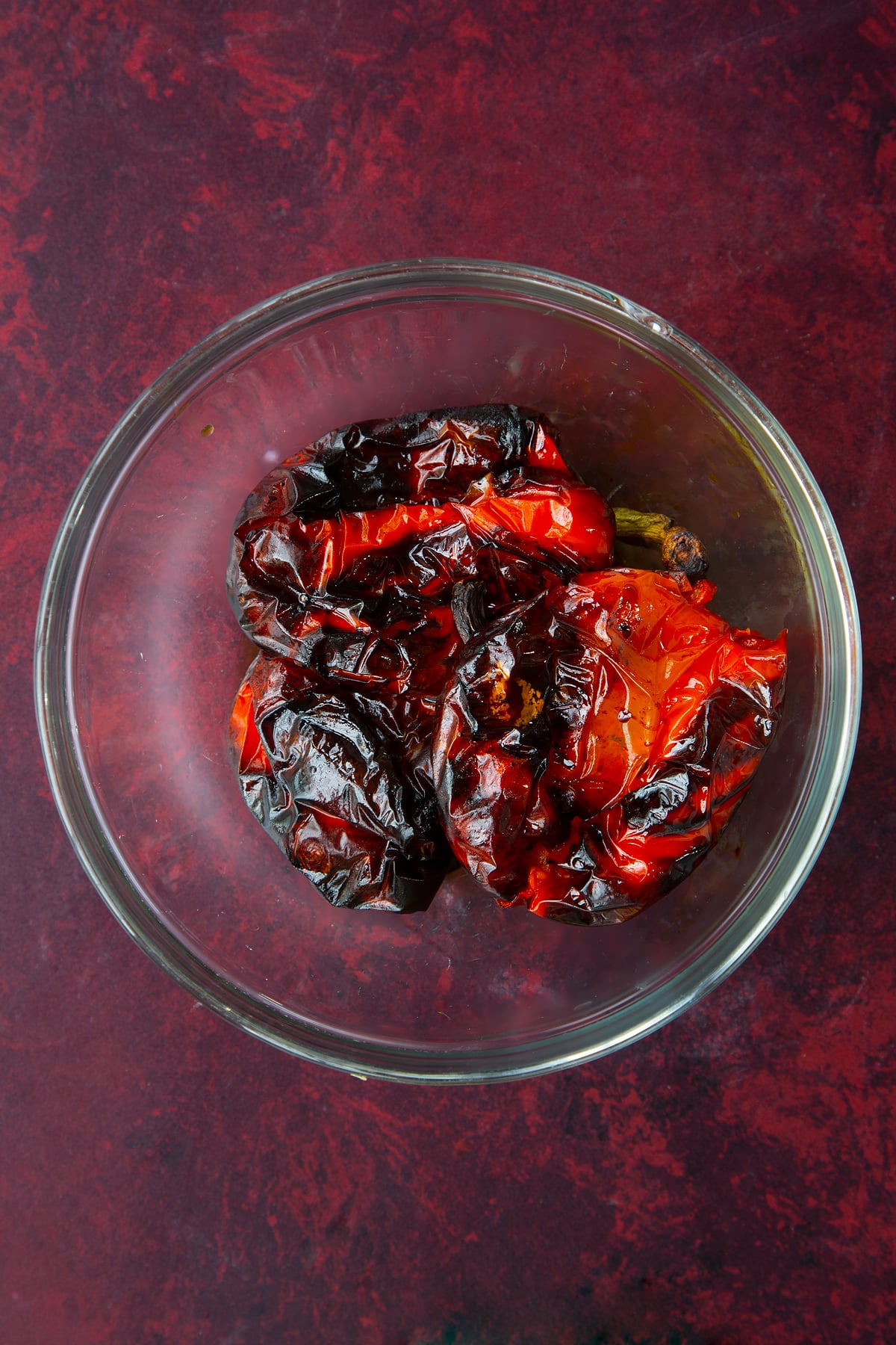 3 whole roasted red peppers in a clear dish.