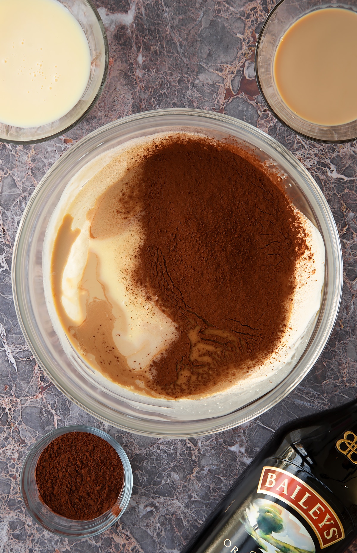 whisked cream topped with condensed milk and Baileys and cococa powder in a large clear bowl.
