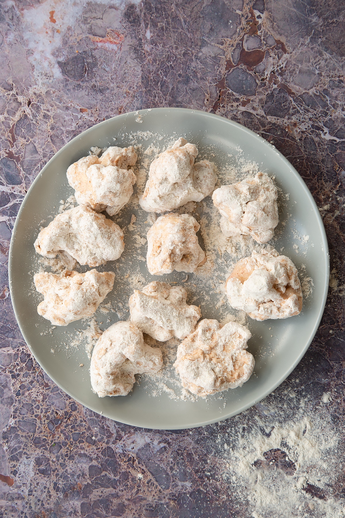 buttermilk marintated cauliflower pieces dusted in spiced flour on a grey plate.