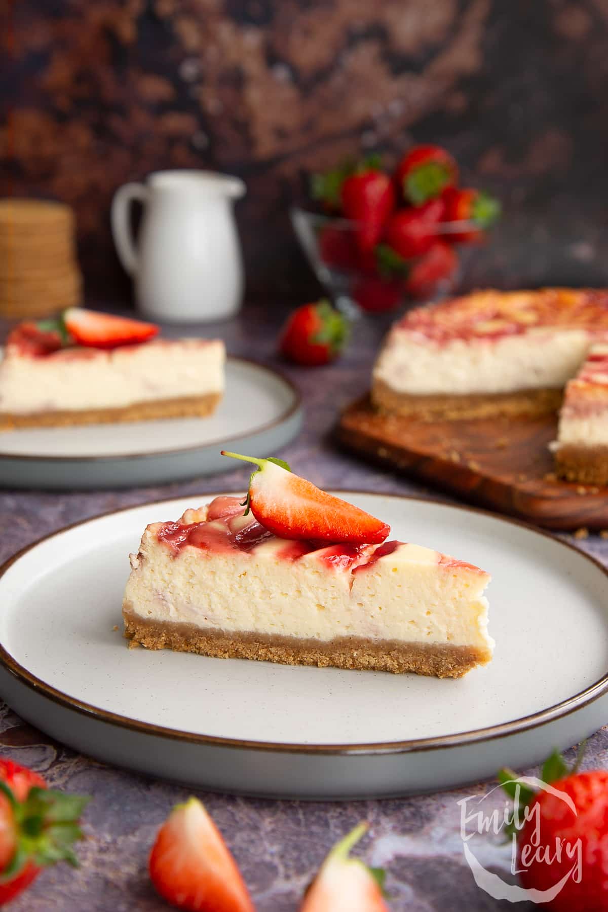 a slice of strawberry swirl cheesecake on a white plate topped with a chopped sttrawberry.