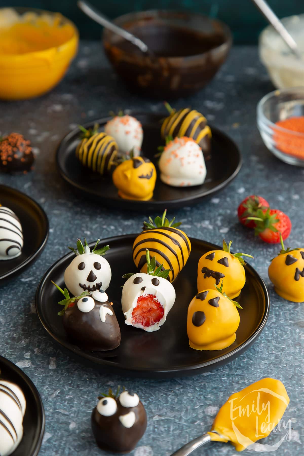 Half eaten halloween chocolate covered strawberries on a dark plate.