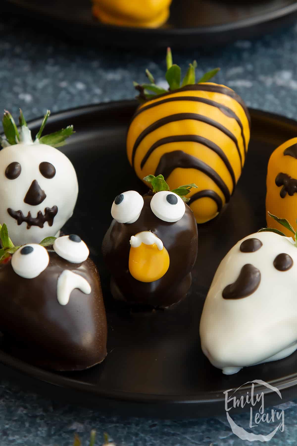 Finished plate of halloween chocolate decorated strawberries on a dark black plate.
