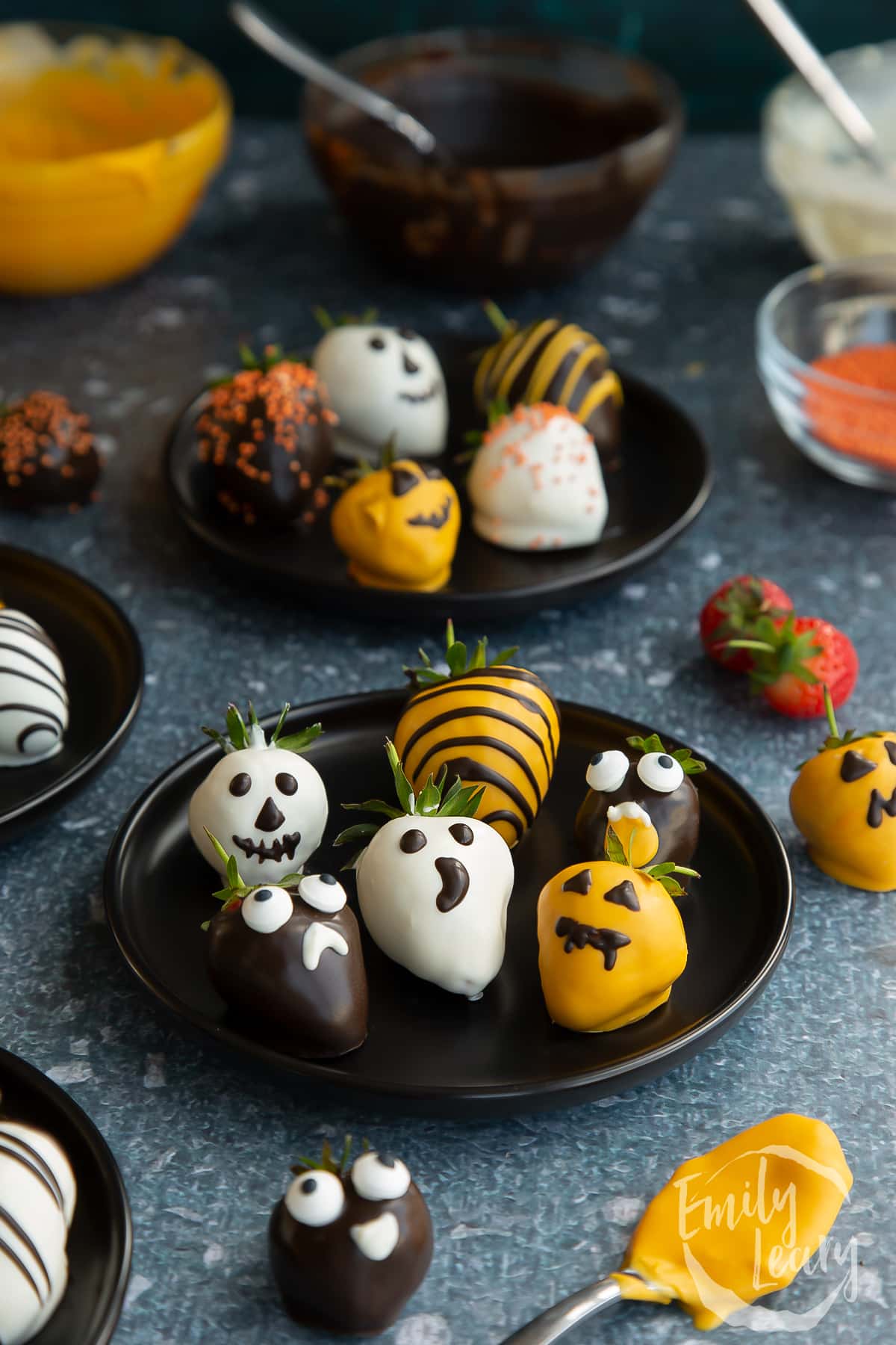 Finished plate of halloween chocolate decorated strawberries on a dark black plate.