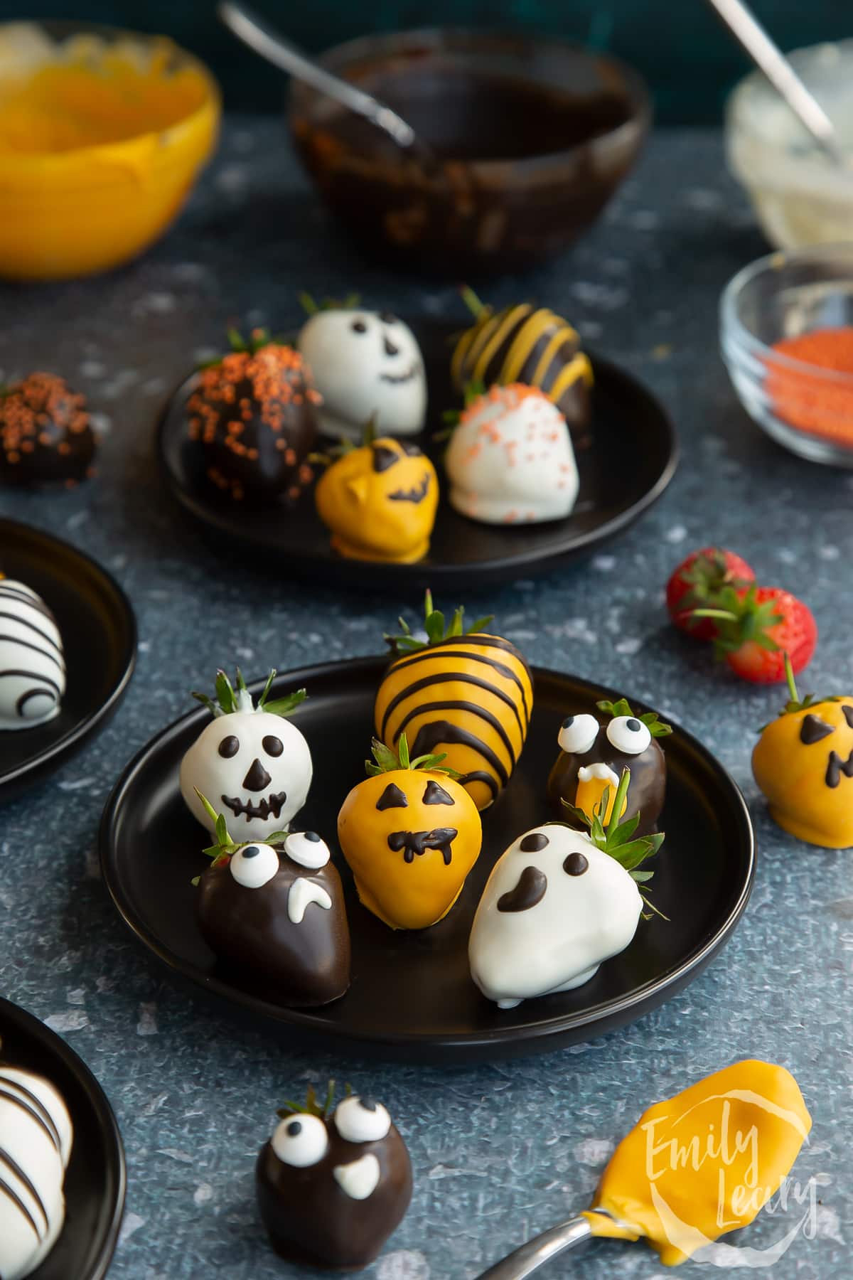 Finished plate of halloween chocolate decorated strawberries on a dark black plate.