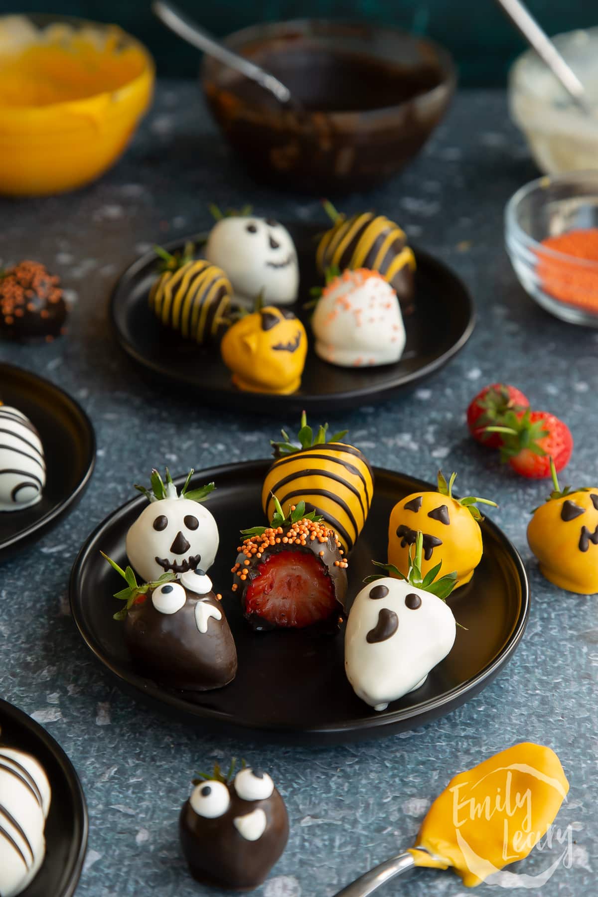 Finished plate of halloween chocolate decorated strawberries on a dark black plate with one having a bite out of it.