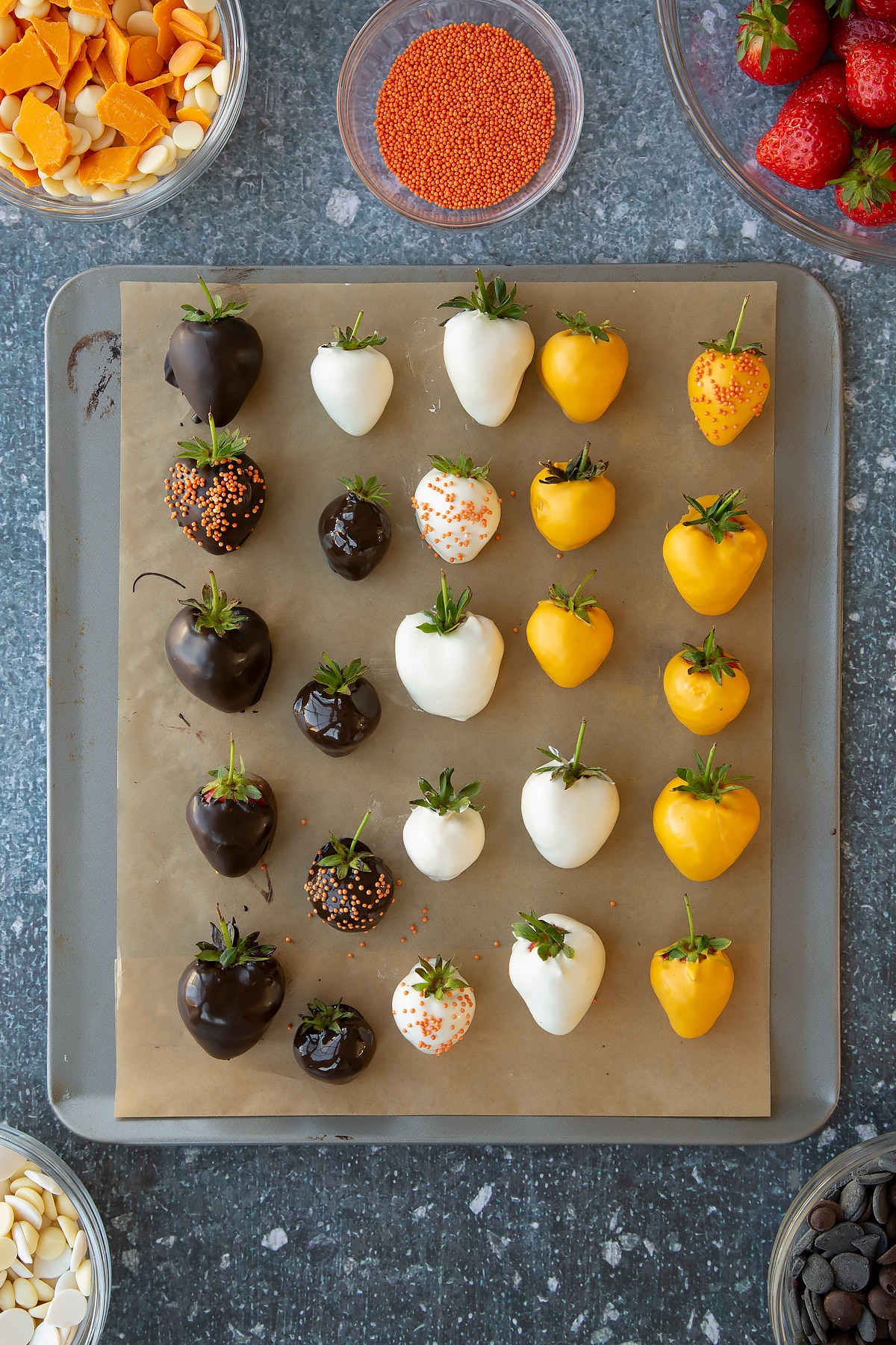 Baking sheet covered in strawberries that have been dipped in the different coloured melted chocolate.